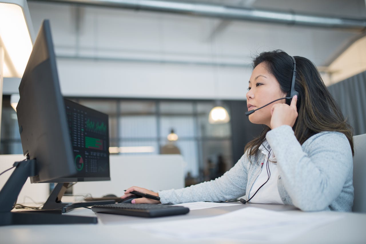 A young Asian woman wearing a headset working on customer support at a modern office desk.